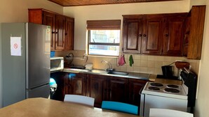A kitchen with wooden cabinets, a refrigerator, a microwave, a sink, a stove, and two chairs. - Spectacular Views of the bay -Bay View Witsand (Witsand)