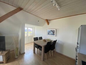 Un coin repas avec une table et des chaises en bois, un téléviseur posé sur un meuble et un tableau encadré accroché au mur.