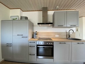 A modern kitchen with grey cabinets, a stainless steel oven, a coffee maker, and a sink. - Koje 2 - Frühstück mit Kutterblick - Ferienwohnungen Meerhuus, 45229 (Jemgum)
