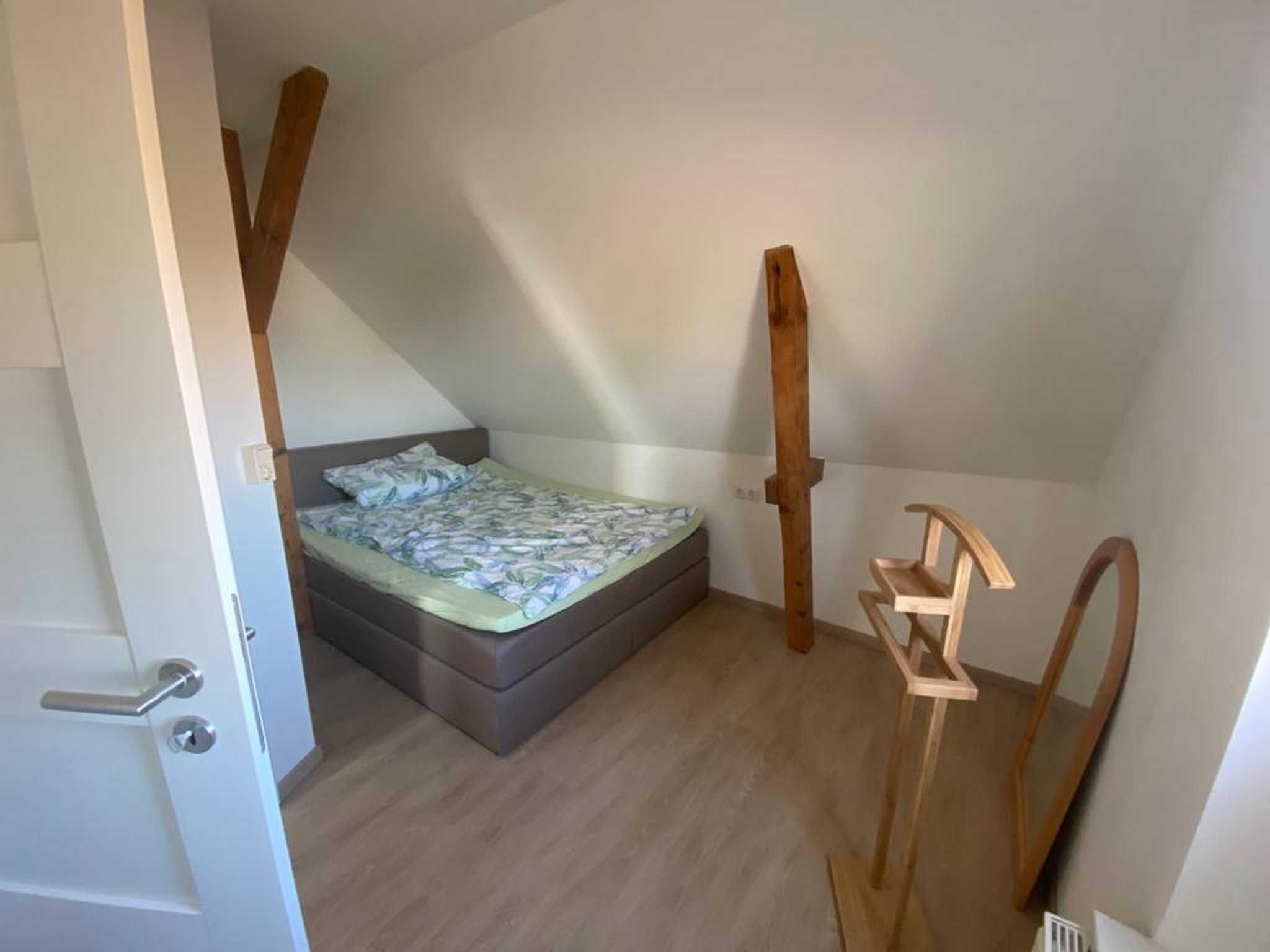 Un dormitorio pequeño con techo inclinado, una cama individual, vigas de madera y una puerta.