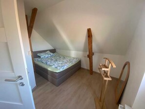 Une petite chambre à coucher avec un plafond en pente, un lit simple, des poutres en bois et une porte.