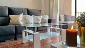 Una sala de estar moderna con un sofá gris oscuro, una mesa de centro de vidrio y una vela encendida sobre una mesa blanca.