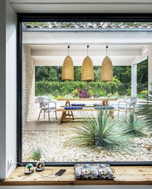 A modern patio with a table and chairs, a hanging light fixture, and a view of a lush garden through a glass door. - Beautiful 4* villa with heated pool - near the beach (La Couarde-sur-Mer)