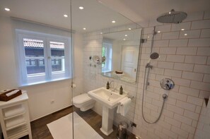 Un baño con inodoro, lavamanos, ducha y mampara de vidrio.
