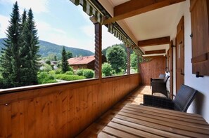 Un balcón de madera con vistas a un paisaje montañoso, una mesa y dos sillas.