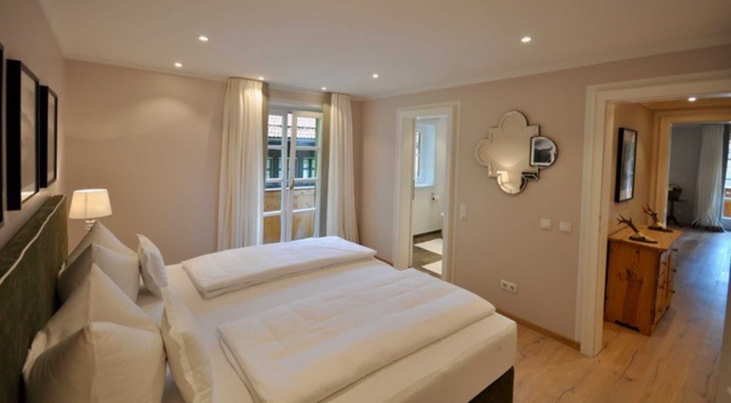 Ein Hotelzimmer mit einem Bett, einem Spiegel, einem Schminktisch und einer Tür, die auf einen Balkon führt.