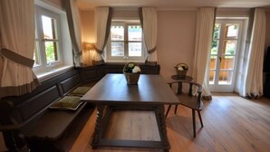 Una habitación con una mesa de madera, bancos y un ventanal con cortinas.