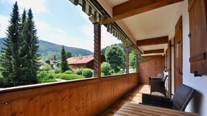 Un balcón de madera con vistas a un paisaje montañoso, una mesa y dos sillas.