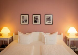 Une chambre d’hôtel avec un lit double, deux lampes de chevet et trois tableaux encadrés au mur.