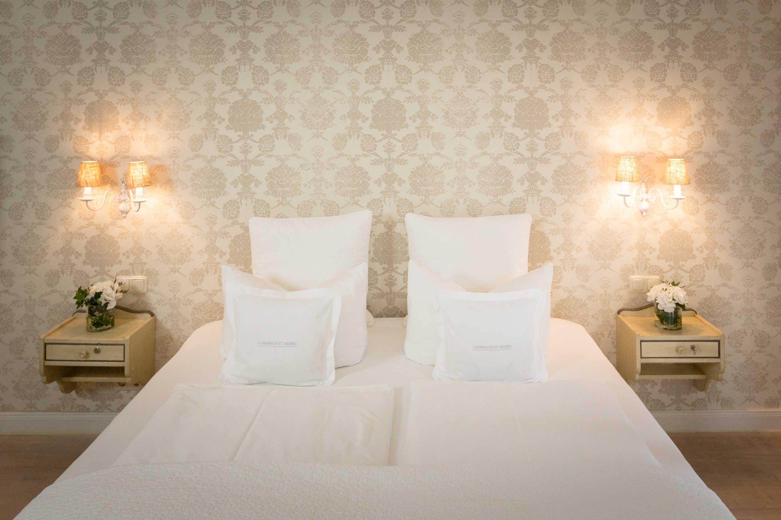 A hotel room with a large bed, two bedside tables, and wall-mounted lamps.