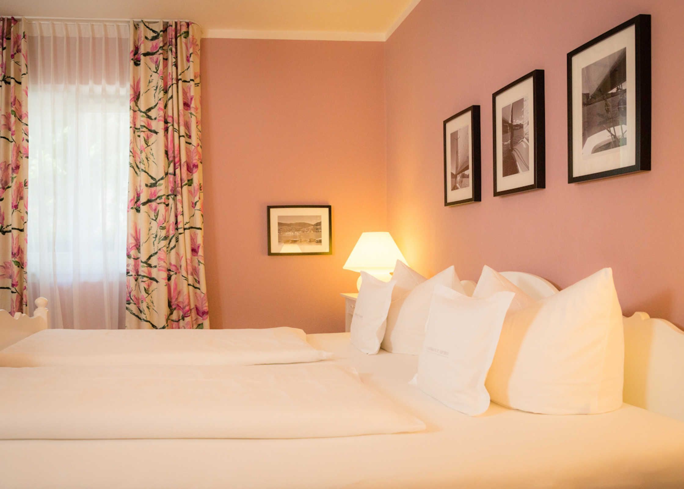 Ein Hotelzimmer mit zwei Betten, einem Nachttisch mit Lampe und drei gerahmten Bildern an der Wand.