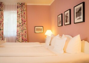 Une chambre d’hôtel avec deux lits, une table de chevet avec une lampe et trois tableaux encadrés au mur.