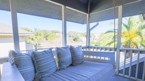 A covered porch with a white cushioned bench, a small table, and a view of palm trees and a beach. - 2 Mins to Beach; Community Pool & Pickleball; Dog Friendly; Walk to Grocery, Shops & Restaurants! (Isle of Palms)