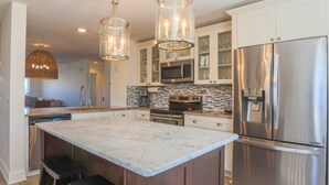 A modern kitchen with a large island, stainless steel appliances, and a unique hanging light fixture. - 2 Mins to Beach; Community Pool & Pickleball; Dog Friendly; Walk to Grocery, Shops & Restaurants! (Isle of Palms)