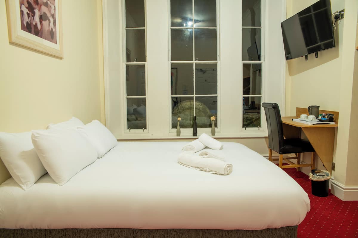 A hotel room with a large bed, a desk with a chair, a TV mounted on the wall, and a window with a view of the outside.