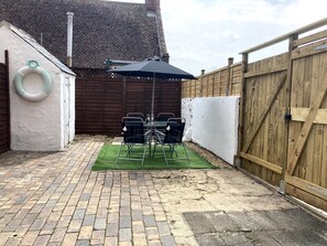 Eine Terrasse mit Ziegelboden, einem Tisch und Stühlen sowie einem schwarzen Sonnenschirm.