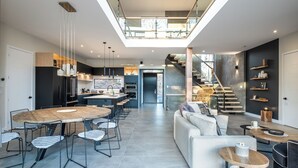 Eine moderne Küche mit Kochinsel, ein Essbereich mit rundem Tisch und Stühlen, eine Treppe, die zu einer oberen Ebene führt, und ein Wohnbereich mit Sofa und Couchtisch.