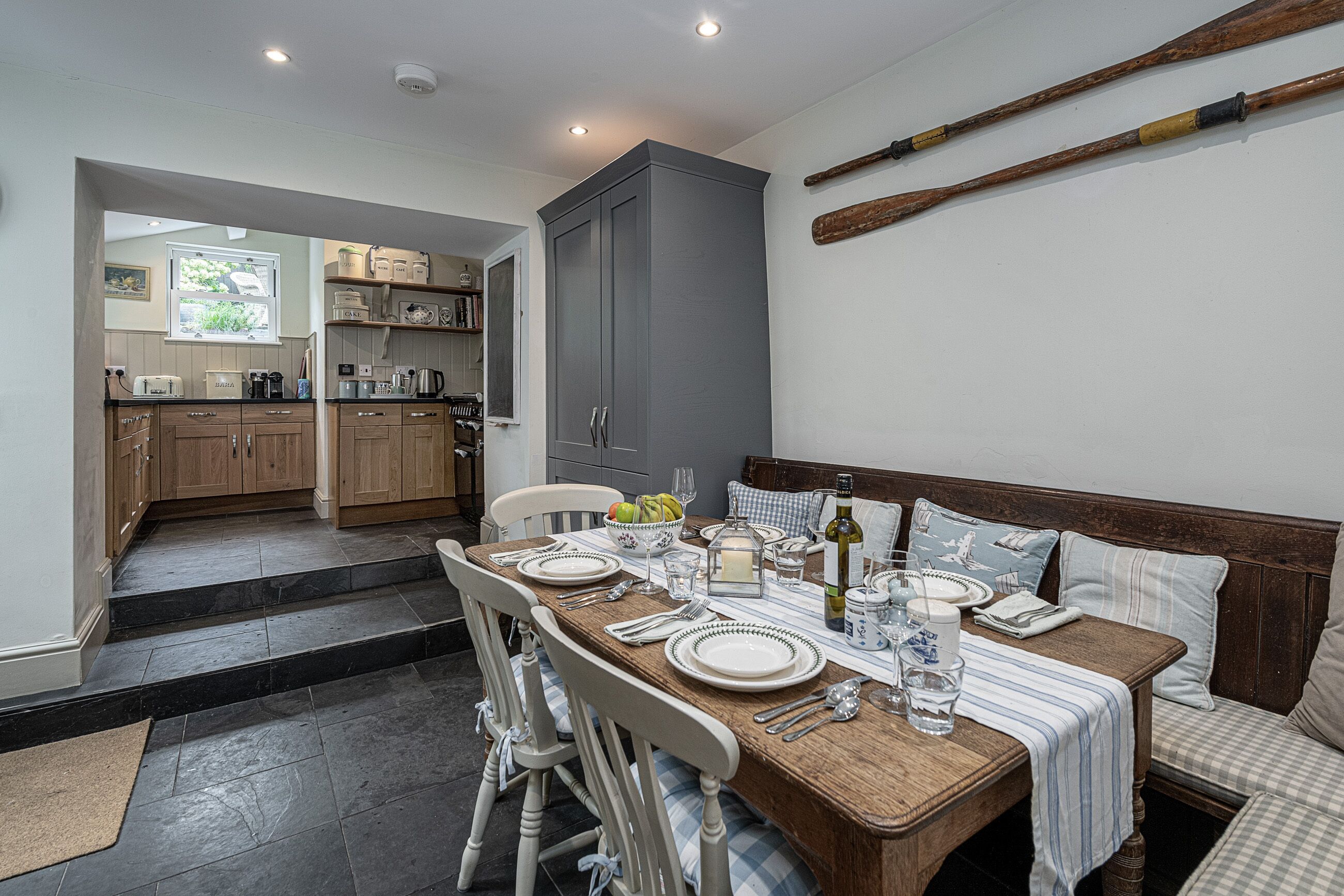 A dining area with a wooden table set for four, a bench with cushions, and a kitchen in the background.