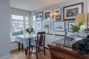 Un coin repas comprenant une table, des chaises, une fenêtre avec des stores et des tableaux encadrés accrochés au mur.