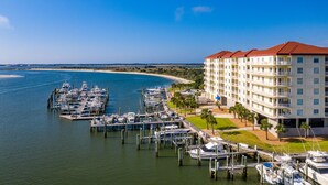 A marina with multiple boats docked, a beachfront hotel with balconies, and a clear blue sky.