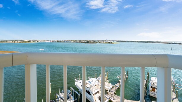 A marina with boats docked, a clear sky, and a distant shoreline.