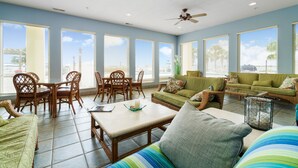 A spacious living room with a dining area, large windows, and a ceiling fan.