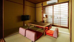 Perinteinen japanilainen huone, jossa on tatamimatto, matala puupöytä ja punaiset tyynyt.