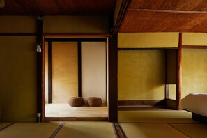 A traditional Japanese room with tatami flooring, a low wooden bed, and two woven baskets. - Kyoto cozy housu 1946 (Kyoto)