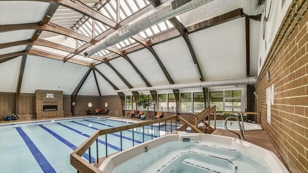 An indoor swimming pool with a hot tub, wooden deck, and brick walls.