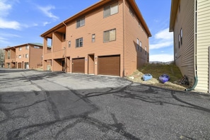A multi-story building with a brick facade, multiple garage doors, and a paved driveway. - Lagoon 736d 2 Bedroom Townhouse by RedAwning (Frisco)