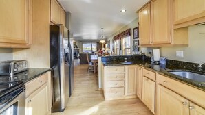 A kitchen with wooden cabinets, a stainless steel refrigerator, a granite countertop, and a sink.
