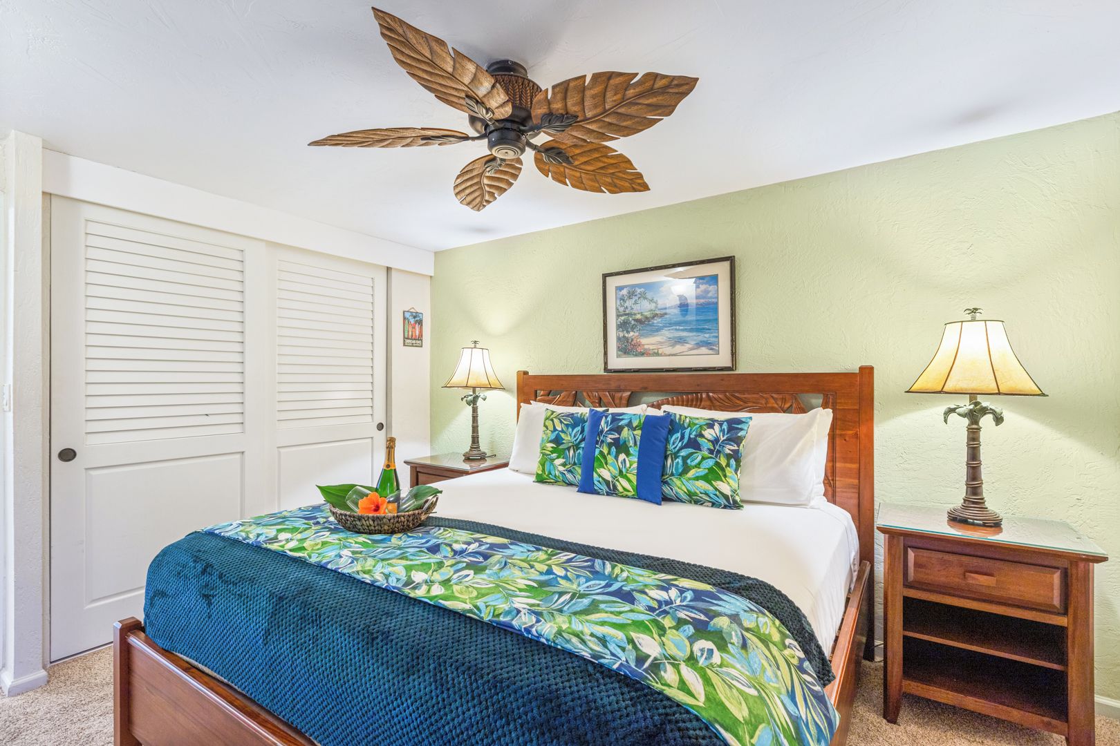 A bedroom with a bed, two bedside tables, a ceiling fan, a framed picture, and a door.