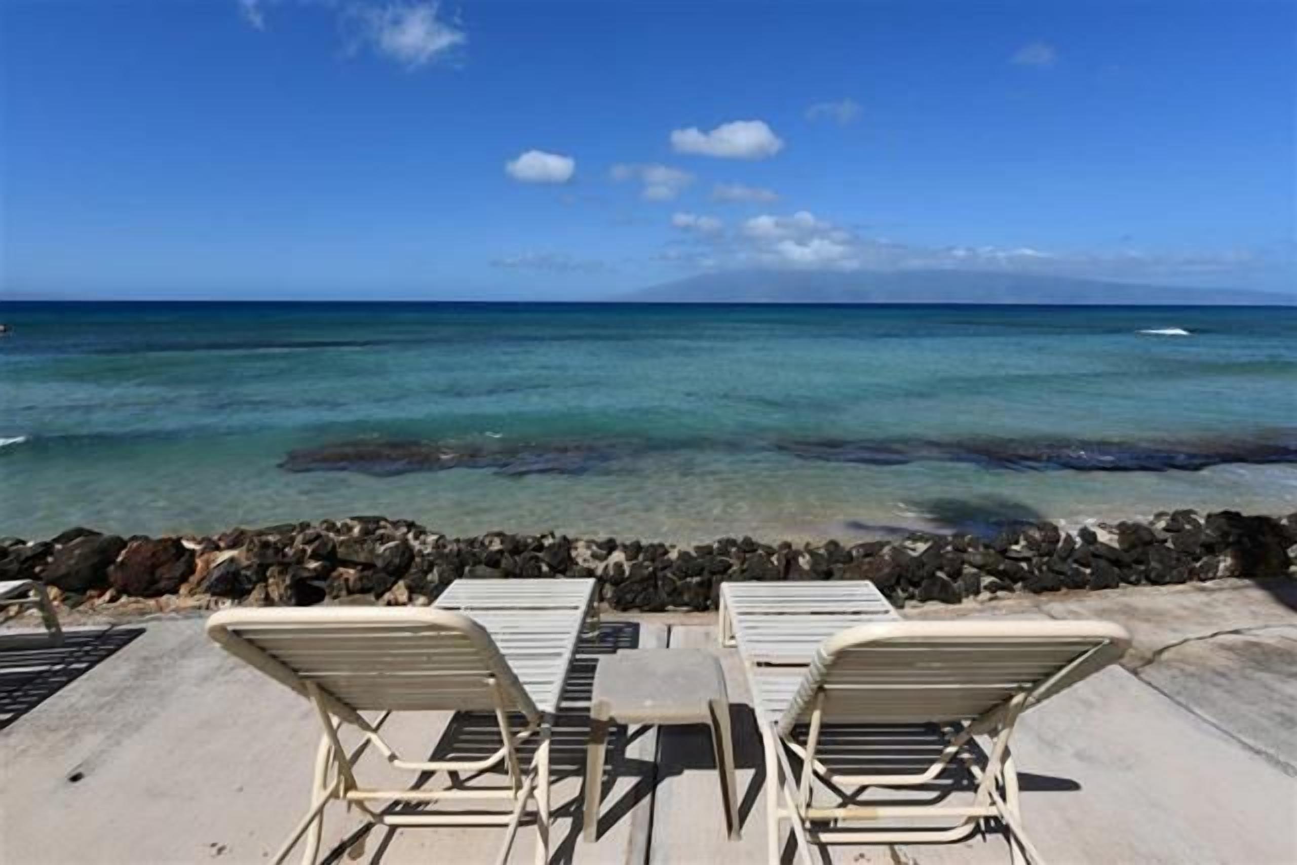 A beachside view with lounge chairs and a rocky shoreline.