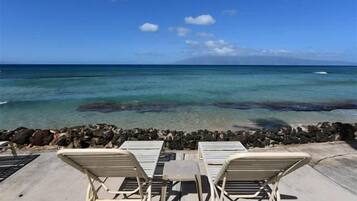 A beachside view with lounge chairs and a rocky shoreline.