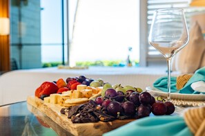 Eine Obstplatte mit Trauben, Erdbeeren und Käse auf einem Holzboden, ein Weinglas und ein Bett mit Blick auf Grünflächen.