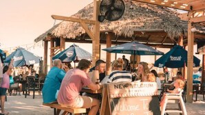 An outdoor seating area with wooden pergolas and thatched roofs, a signboard for New Belgium Brewing, and people dining. - Bohemian Sunrise  (Englewood)