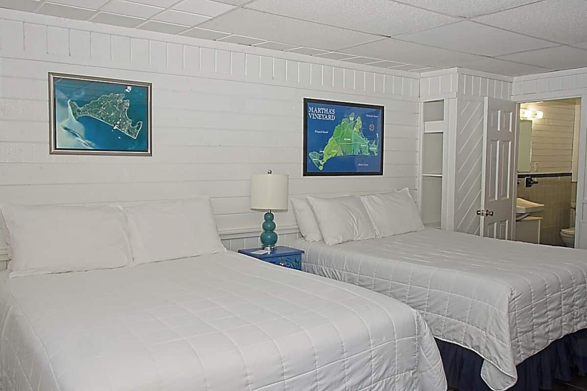 A hotel room with two beds, a nightstand with a lamp, and two framed maps on the wall.