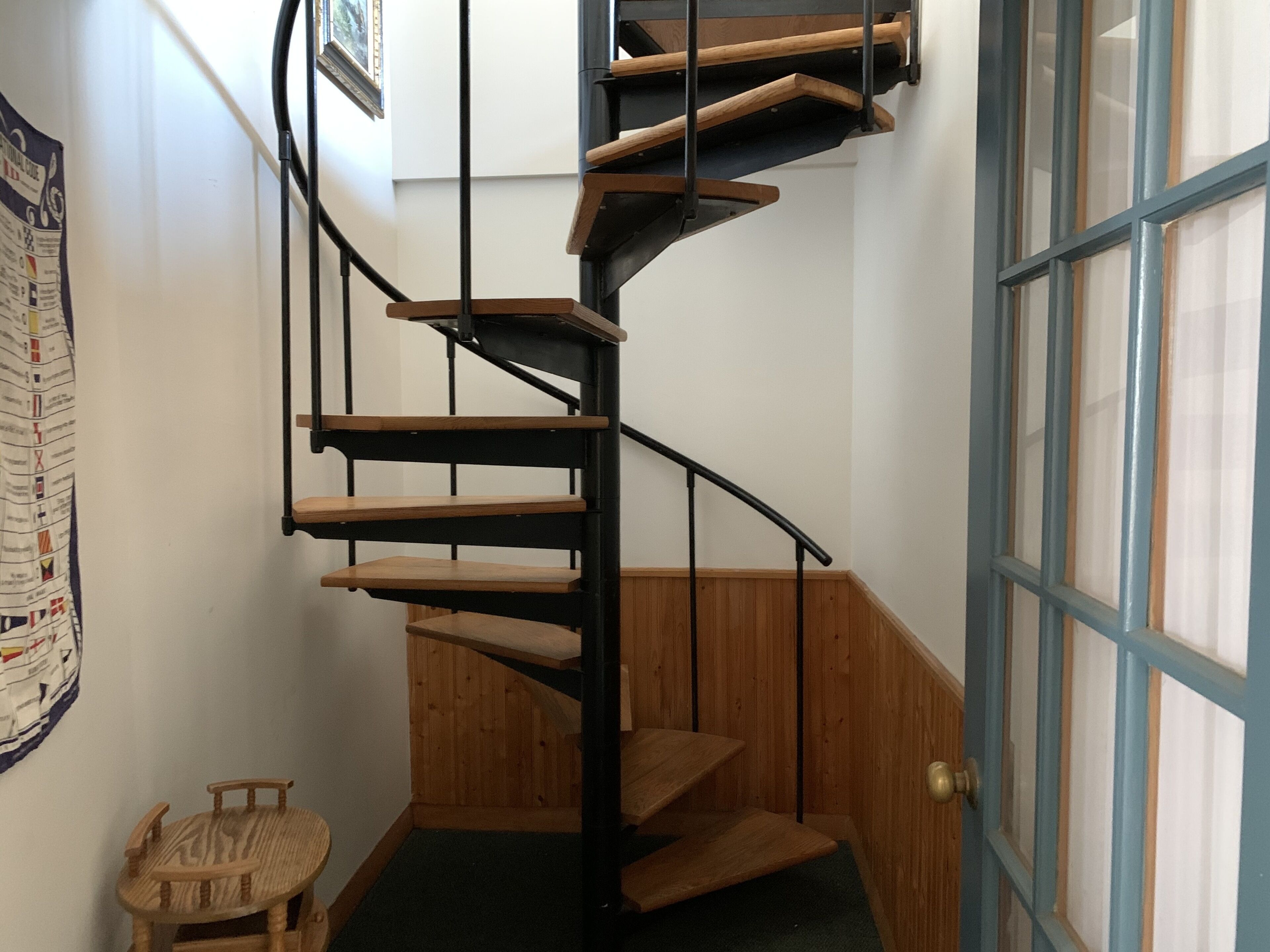 Eine Wendeltreppe mit Holzstufen und schwarzen Metallgeländern, die zu einer Tür mit blau-weißen Feldern führt.