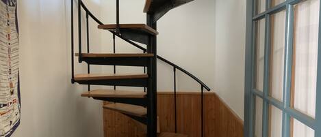 A spiral staircase with wooden steps and black metal railings, leading to a door with blue and white panels.