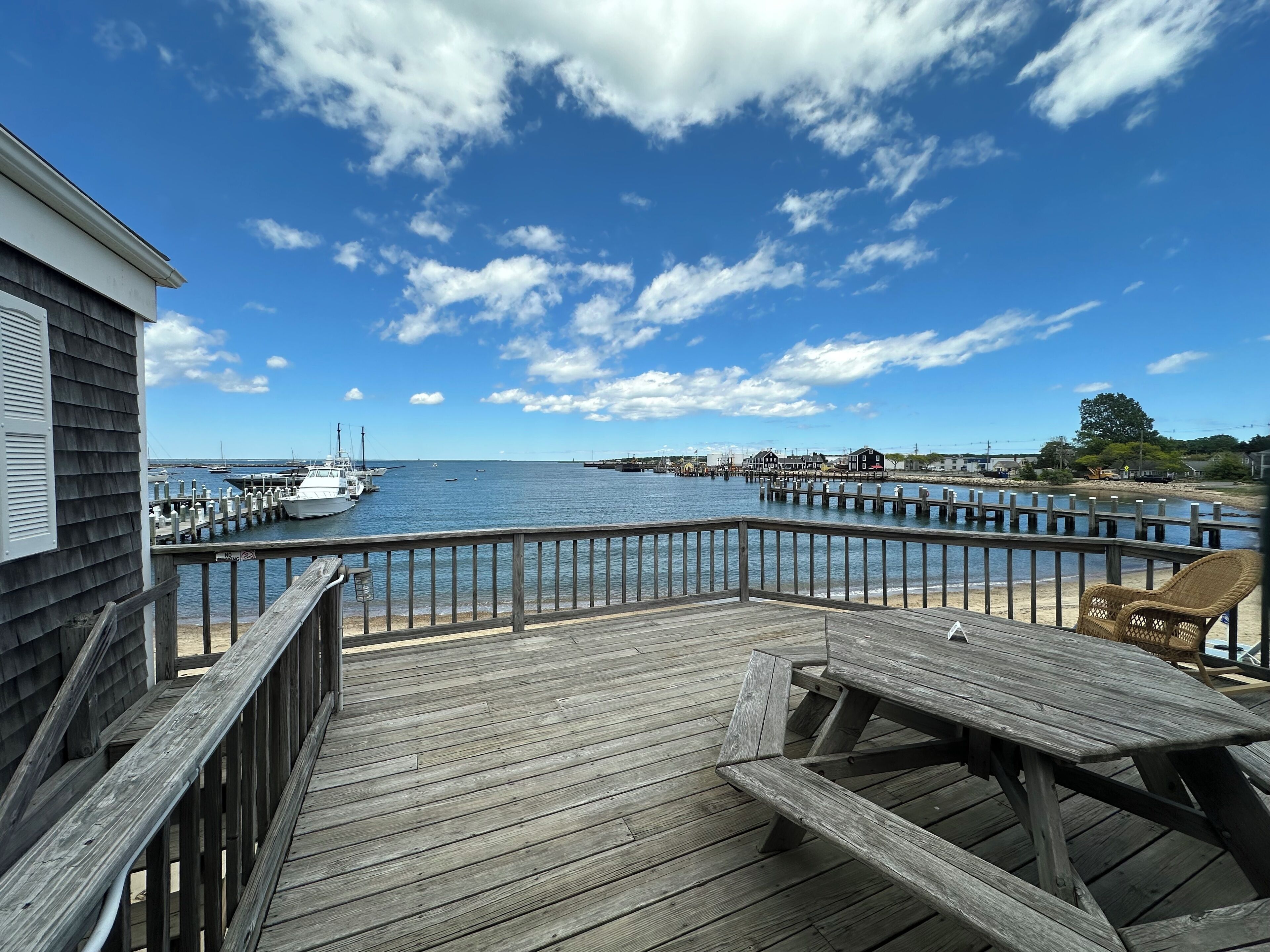 A wooden deck with picnic tables overlooking a marina with boats and a pier extending into the water.