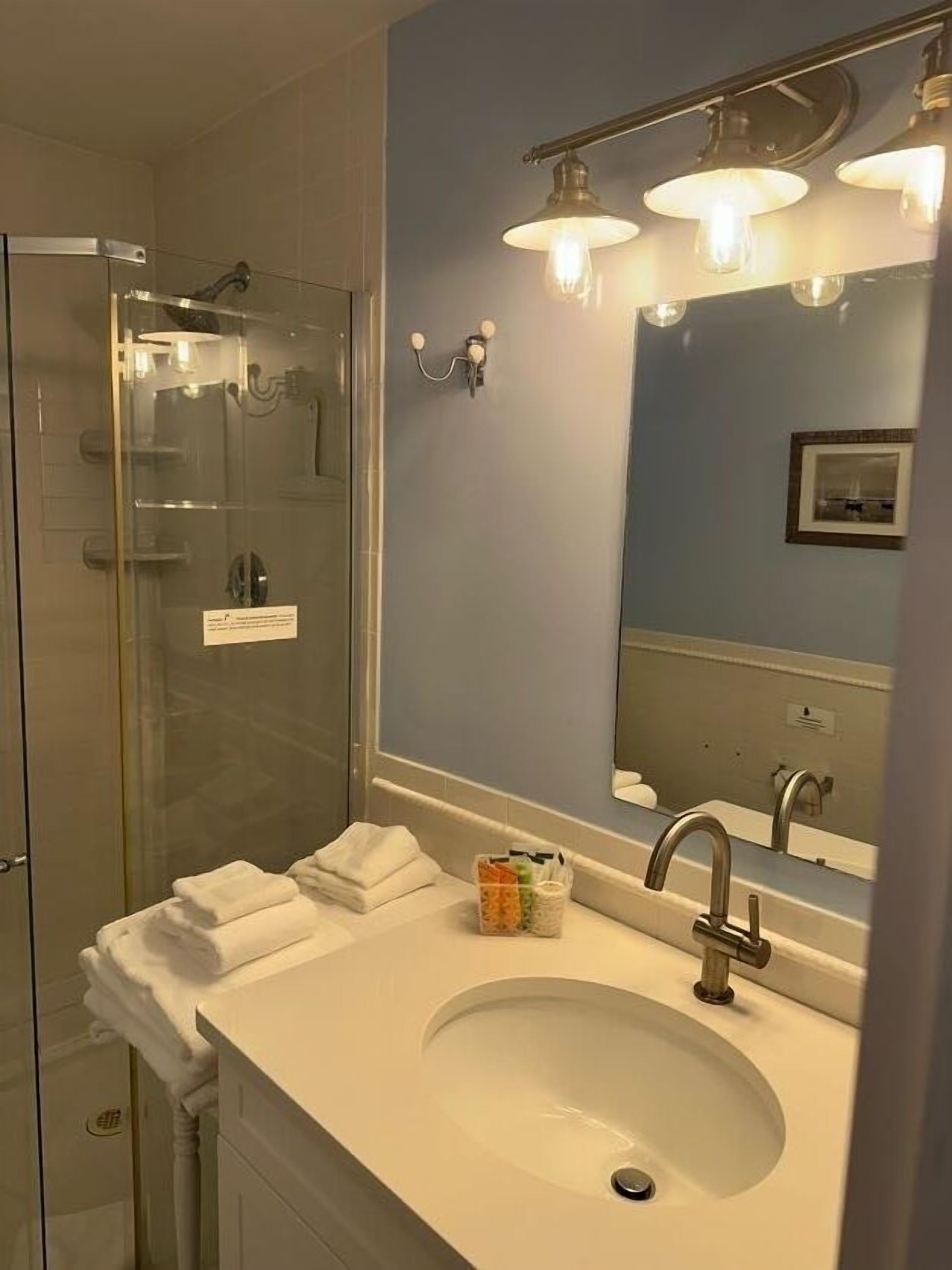 A bathroom with a glass shower enclosure, a white sink with a mirror above it, and a towel rack with folded towels.