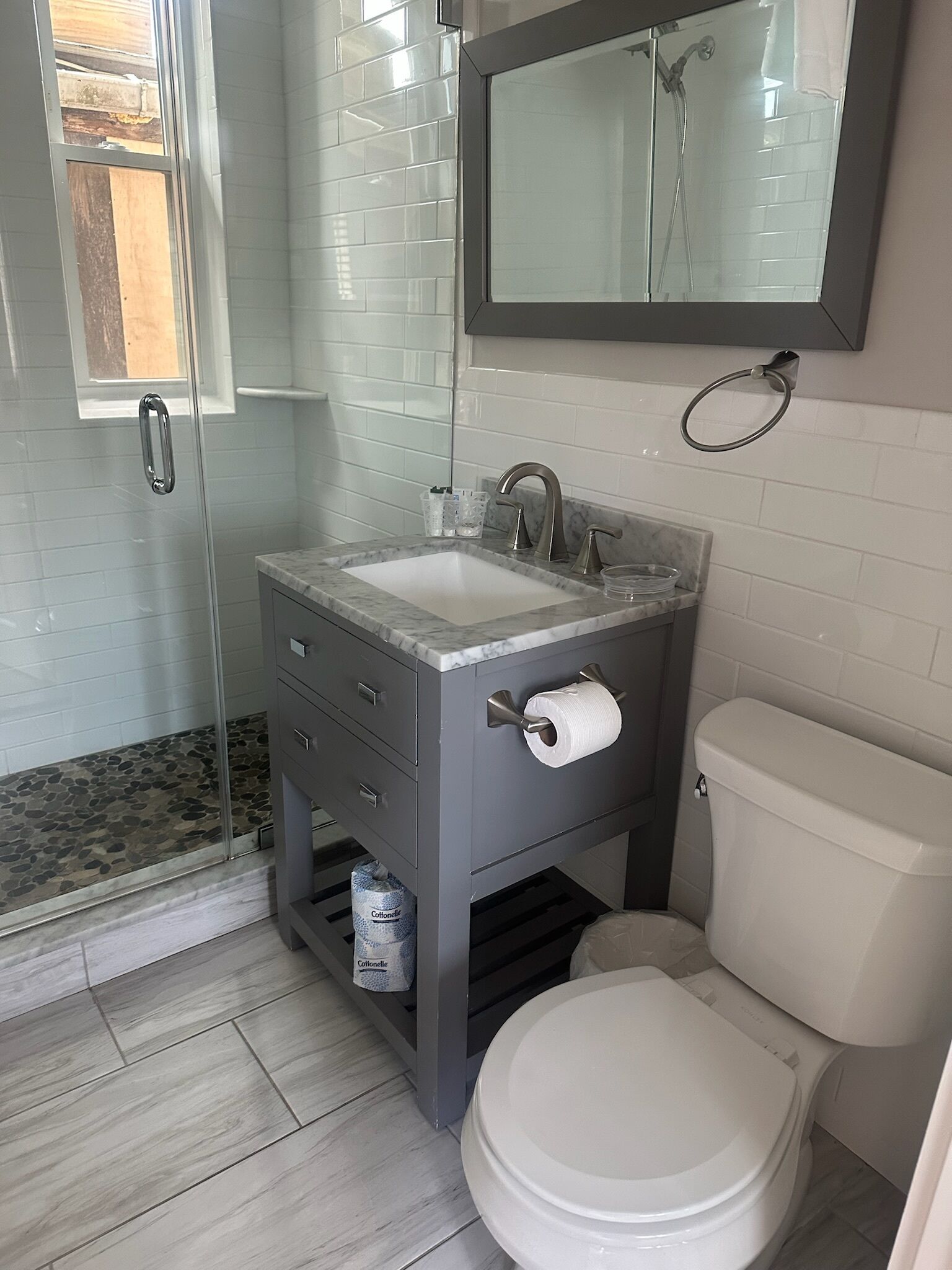 A bathroom with a glass shower enclosure, a marble sink, a toilet, and a mirror above the sink.