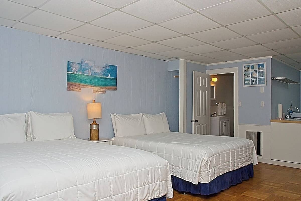 A bedroom with two beds, a nightstand with a lamp, a painting on the wall, and a bathroom visible through an open door.