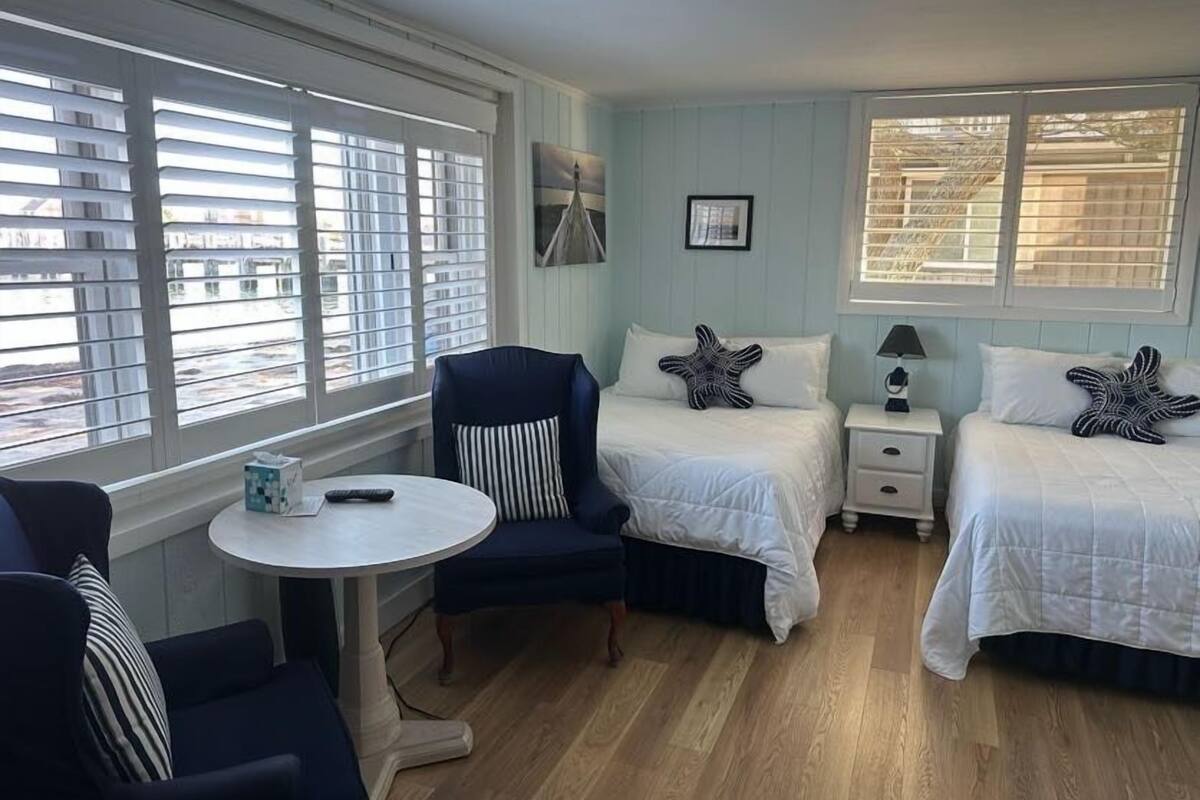 A room with two beds, a chair, a small table, and a nightstand.