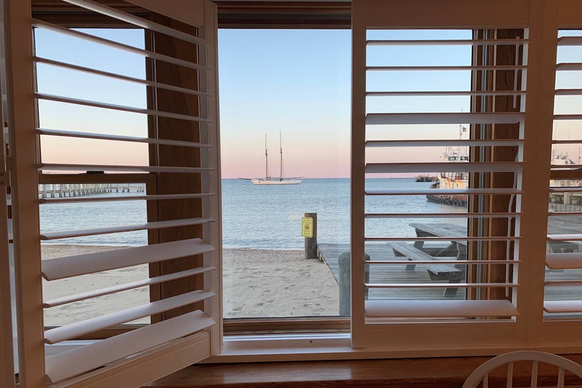 A room with a view of a beach, a pier, and a sign indicating no swimming.