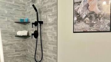 A shower with a glass door, a towel rack, and a shelf with toiletries.