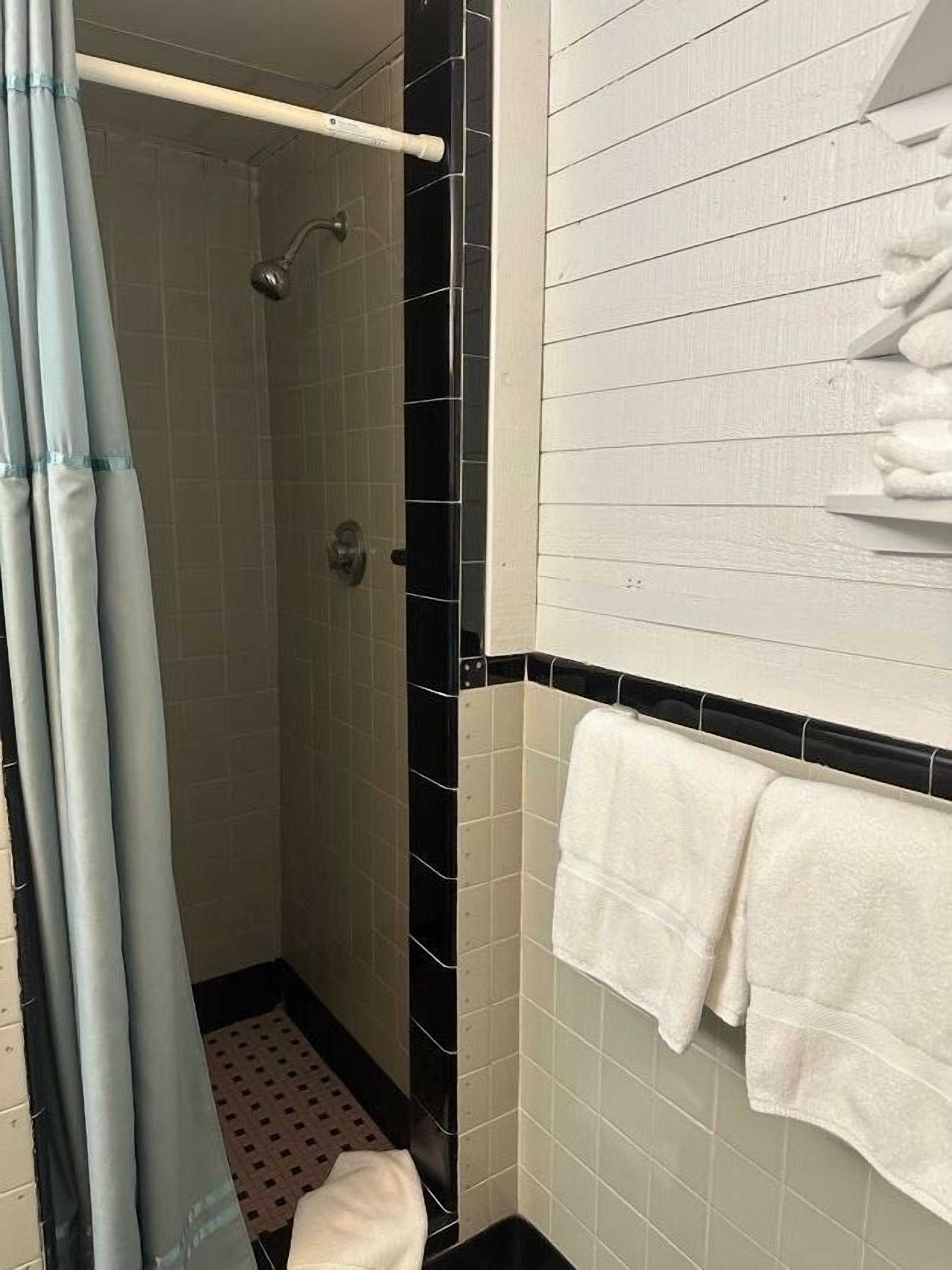Un baño con ducha, paredes de azulejos y un perchero con toallas.