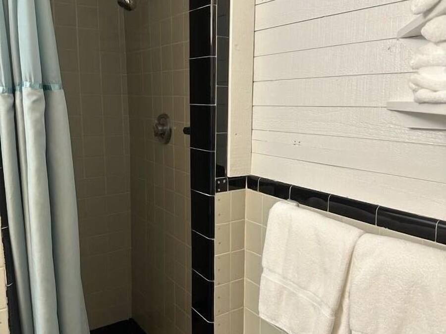 Un baño con ducha, paredes de azulejos y un perchero con toallas.