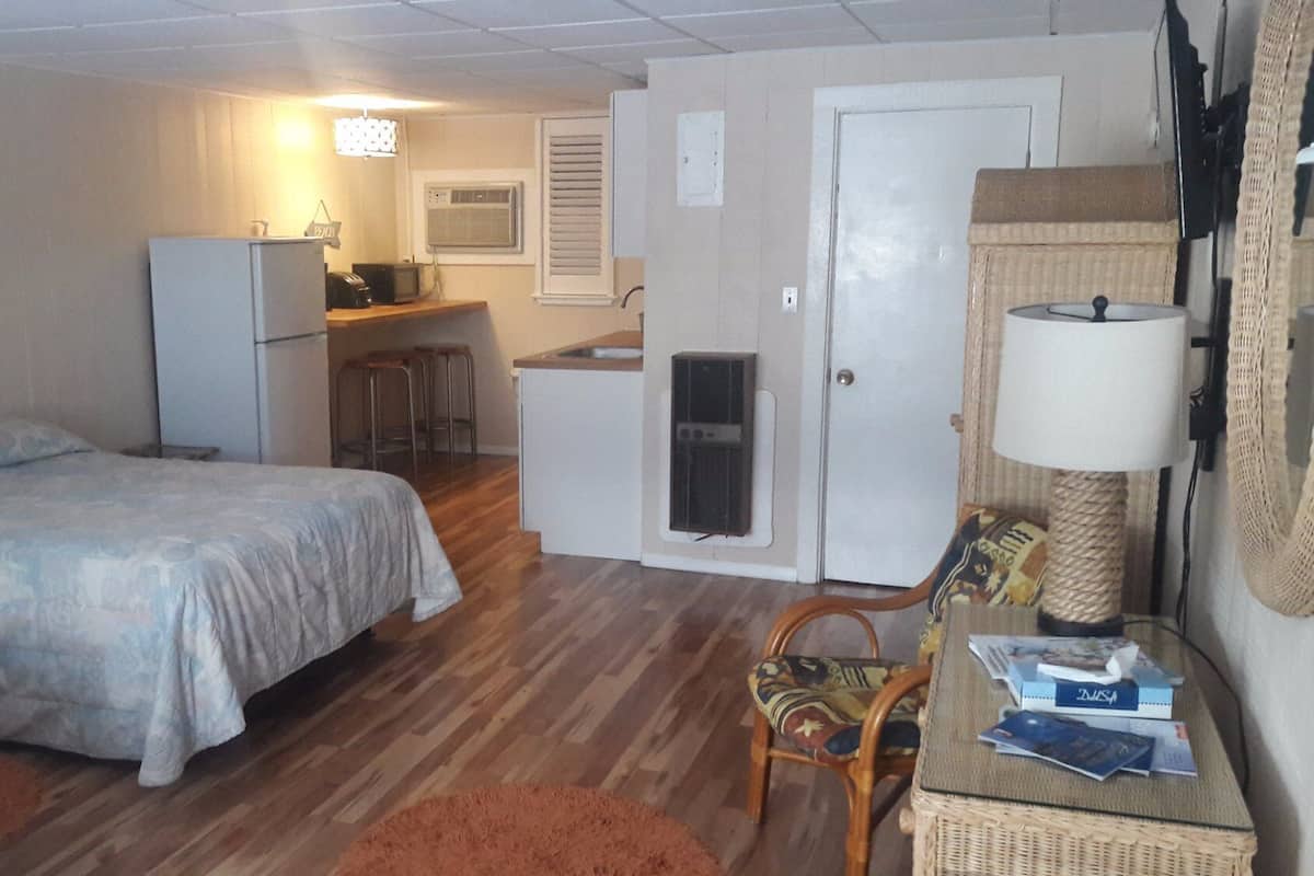 A compact room with a bed, kitchenette, and a small seating area.