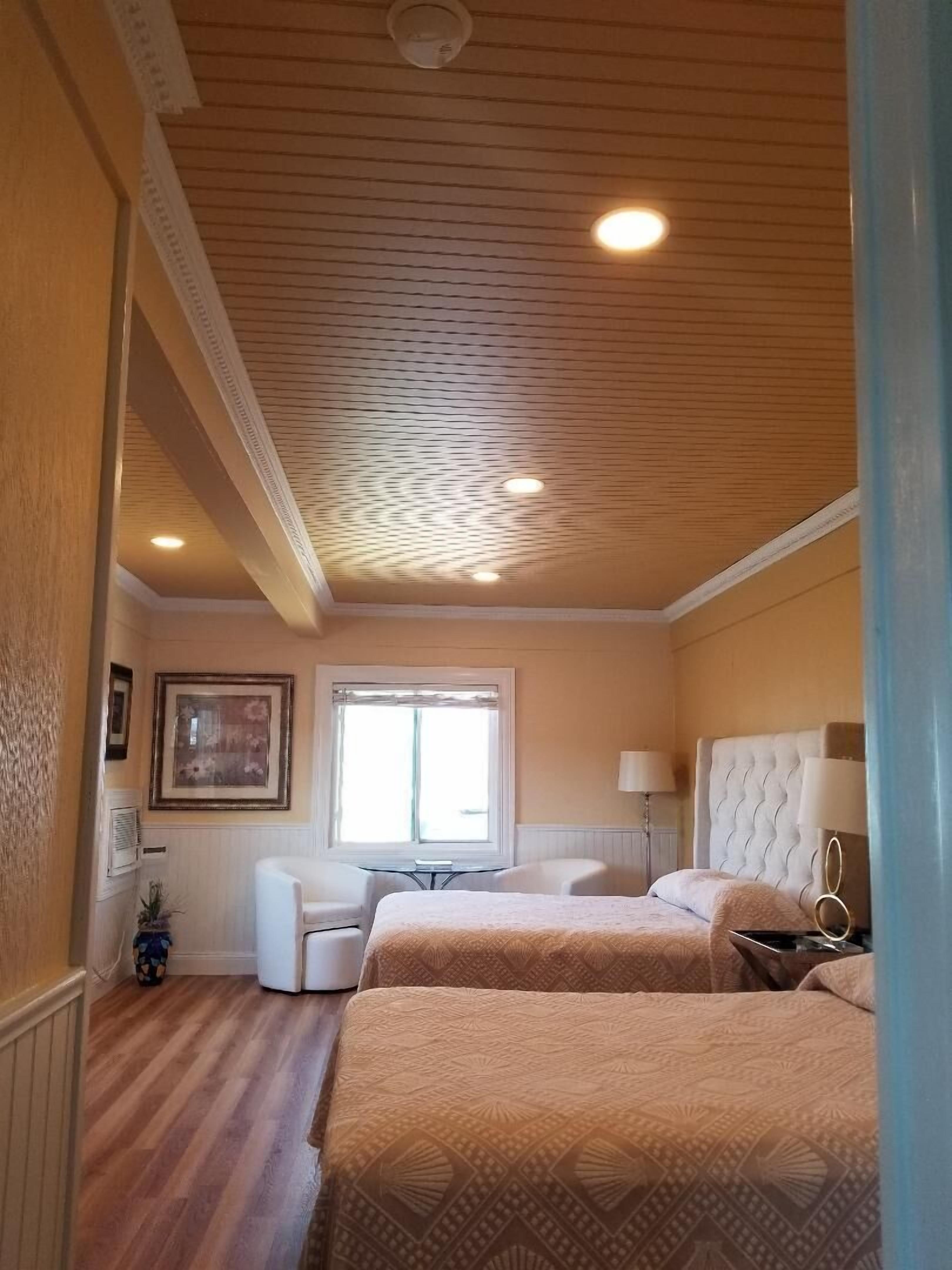 A hotel room with two beds, a window, a desk, and a chair.